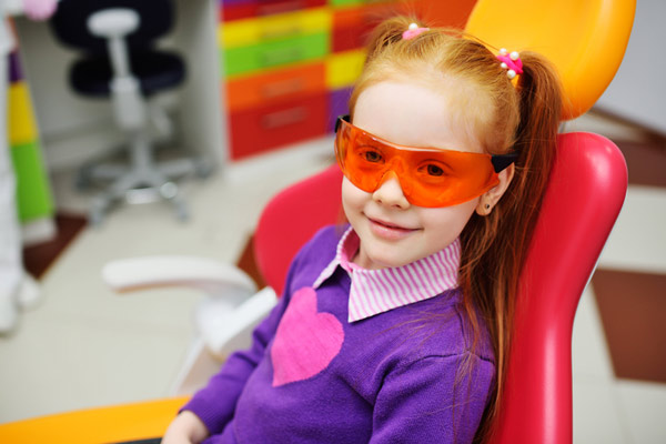 Young red headed girl with pigtails smiling in dental chair.